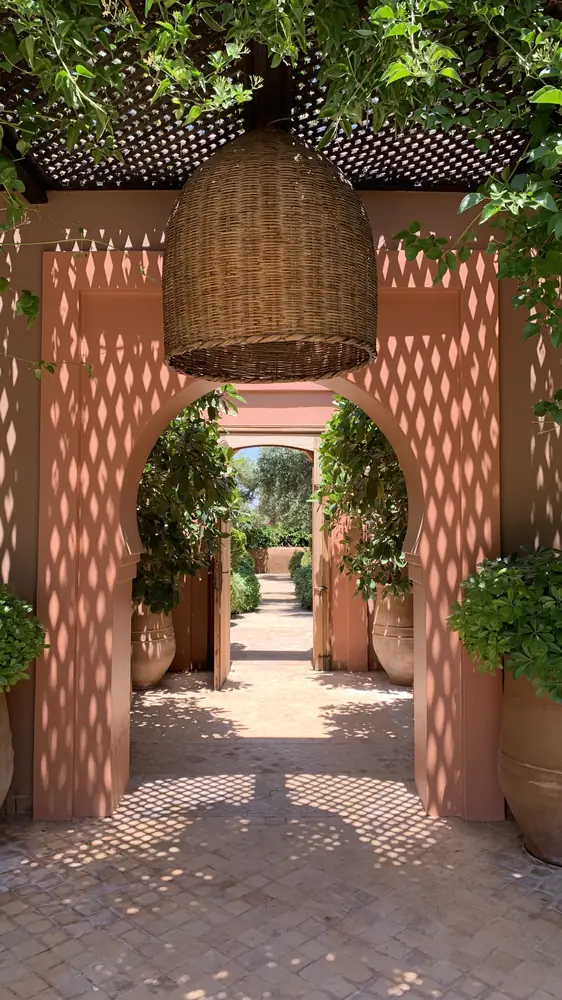 Arche rose sous une lanterne en osier, et le jardin au loin